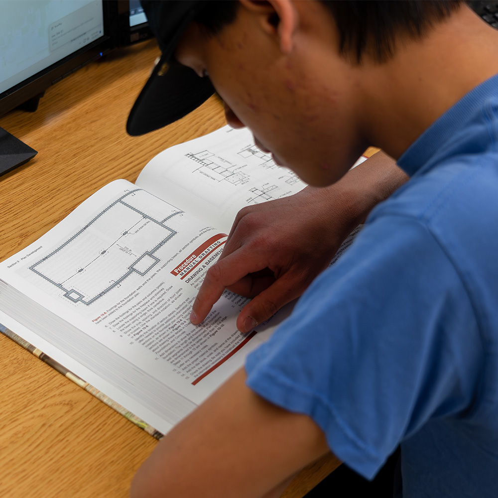 An engineering student studying a book about CAD